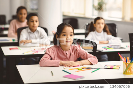 Return Back To School. Portrait of focused diligent asian female pupil sitting with folded arms at desk with group of diverse classmates, listening to teacher, selective focus. Academic Concept Return Back To School. Portrait of focused diligent asian female pupil sitting with folded arms at desk with group of diverse classmates, listening to teacher, selective focus. Academic Concept 134067006