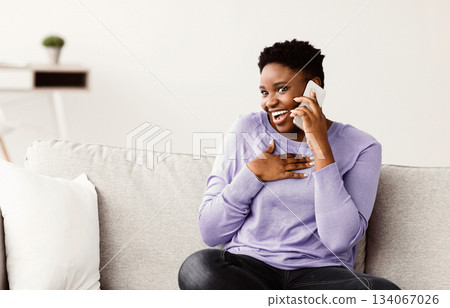 Good Talk With Boyfriend Or Friend. Cheerful young chubby african american lady answering and making call on her smartphone, hearing news or gossips, sitting on the couch in living room at home 134067026