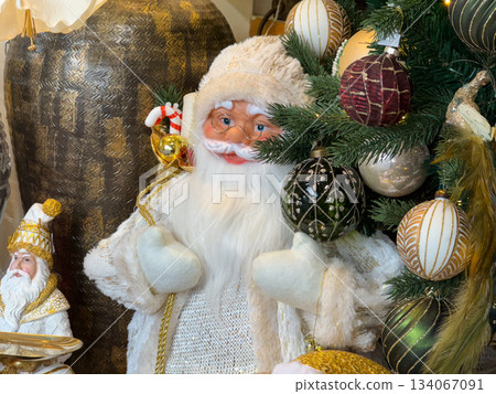 Elegant white Santa figure beside decorated Christmas tree with golden ornaments. Festive luxury, warm winter celebration, nostalgia and traditional holiday joy Elegant white Santa figure beside decorated Christmas tree with golden ornaments. Festive luxury, warm winter celebration, nostalgia and traditional holiday joy 134067091