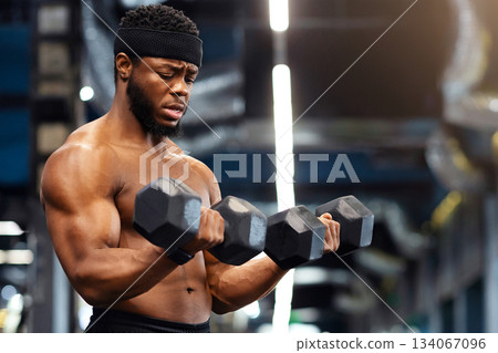 Handsome african american shirtless bodybuilder making work out with barbells at gym, copy space. Hot black guy exercising with two dumbbells, working on his muscular biceps Handsome african american shirtless bodybuilder making work out with barbells at gym, copy space. Hot black guy exercising with two dumbbells, working on his muscular biceps 134067096