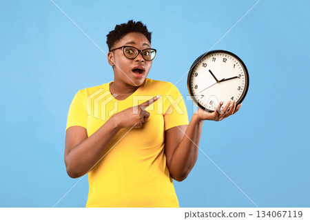 Deadline, Time Is Over. Oversized African Woman Showing Clock Posing Standing Over Blue Studio Background, Looking At Camera. Shocked Black Lady Being Late. Time's Tickling Concept Deadline, Time Is Over. Oversized African Woman Showing Clock Posing Standing Over Blue Studio Background, Looking At Camera. Shocked Black Lady Being Late. Time's Tickling Concept 134067119
