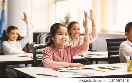 Concept of School Reopen, Back To Normal Lifestyle. Intelligent group of young multiethnic schoolchildren all raising their hands up in the air to answer a question, selective focus on asian girl Concept of School Reopen, Back To Normal Lifestyle. Intelligent group of young multiethnic schoolchildren all raising their hands up in the air to answer a question, selective focus on asian girl 134067148