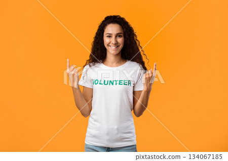 Smiling Volunteer Woman Pointing Fingers Upward Looking At Camera Standing In Studio Over Yellow Background. Look Up Concept, Volunteering Advertisement Smiling Volunteer Woman Pointing Fingers Upward Looking At Camera Standing In Studio Over Yellow Background. Look Up Concept, Volunteering Advertisement 134067185