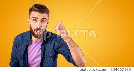 Portrait of young angry guy shaking clenched fist at camera and shouting, showing his protest over orange studio background. Furious millennial man threatening someone, expressing negativity 134067189