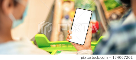 Grocery Shopping Mobile App. Back View Of Black Couple Holding Smartphone With Empty Screen Buying Food Online In Application, Walking With Trolley Cart Full Of Products In Supermarket. Panorama Grocery Shopping Mobile App. Back View Of Black Couple Holding Smartphone With Empty Screen Buying Food Online In Application, Walking With Trolley Cart Full Of Products In Supermarket. Panorama 134067201