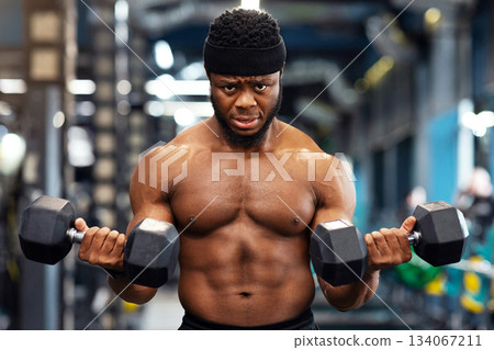 Muscular black guy doing workout with dumbbells at gym, lifting weight with both hands, copy space. Motivated african american man bodybuilder working on biceps, weight exercises concept Muscular black guy doing workout with dumbbells at gym, lifting weight with both hands, copy space. Motivated african american man bodybuilder working on biceps, weight exercises concept 134067211