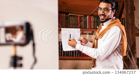 Arab Teacher Man Making Video Lecture Teaching And Explaining English Grammar Rules Online Standing Near Blackboard At Home. Educational Blog, Remote Education, E-Teaching And E-Learning 134067257