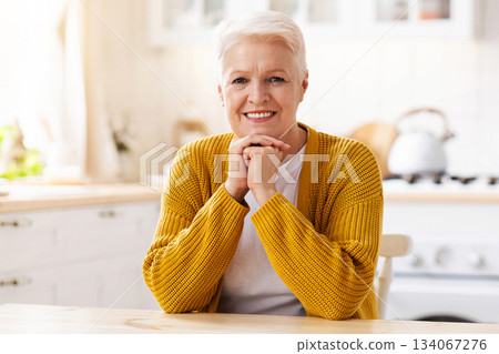 Portrait of happy old woman sitting in cozy kitchen and smiling at camera, copy space. Positive senior beautiful lady posing at home, resting alone after cooking. Life after retirement Portrait of happy old woman sitting in cozy kitchen and smiling at camera, copy space. Positive senior beautiful lady posing at home, resting alone after cooking. Life after retirement 134067276
