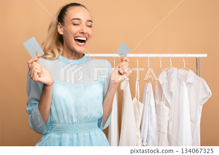 Time For Shopping Concept. Portrait of excited young woman holding and showing two debit credit cards, standing in wardrobe near clothing rail and screaming yes with joy, happy about purchases Time For Shopping Concept. Portrait of excited young woman holding and showing two debit credit cards, standing in wardrobe near clothing rail and screaming yes with joy, happy about purchases 134067325
