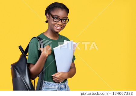 Cheerful African American Female Student Posing Holding Notebooks Smiling To Camera Standing In Studio Over Yellow Background. Students Lifestyle, University And College Education Concept Cheerful African American Female Student Posing Holding Notebooks Smiling To Camera Standing In Studio Over Yellow Background. Students Lifestyle, University And College Education Concept 134067388