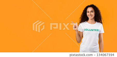 Cheerful Volunteer Lady Pointing Finger Aside At Free Space Advertising Text Standing Over Yellow Background. Female Activist Advertising Your Text. Panorama, Studio Shot 134067394