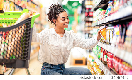 African Woman Buyer Choosing Products Doing Grocery Shopping Buying Healthy Organic Food In Local Supermarket, Posing With Shop Cart Full Of Groceries. Happy Female Customer Concept 134067432