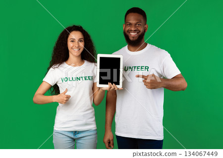 Diverse Volunteers Holding Digital Tablet Pointing At Blank Computer Screen And Gesturing Thumbs Up Standing In Studio On Green Background, Smiling To Camera. Mockup Diverse Volunteers Holding Digital Tablet Pointing At Blank Computer Screen And Gesturing Thumbs Up Standing In Studio On Green Background, Smiling To Camera. Mockup 134067449