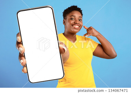 Call Me. Positive Plus Size African Woman Holding Hand Near Ear Like Phone And Pointing Finger At Camera Recommending To Contact Her Standing Over Blue Background. Studio Shot 134067471