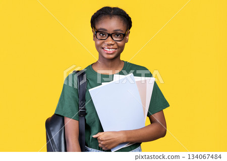 Happy Black Female Student Posing With Books And Notebooks Standing On Yellow Studio Background, Smiling To Camera. College And University Education, Students Lifestyle Concept 134067484