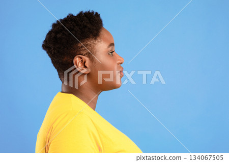 Profile Portrait Of Overweight African American Woman With Short Haircut Posing Looking Aside Over Blue Studio Background. Side-View Shot Of Plus Size Black Female. Empty Space For Text Profile Portrait Of Overweight African American Woman With Short Haircut Posing Looking Aside Over Blue Studio Background. Side-View Shot Of Plus Size Black Female. Empty Space For Text 134067505