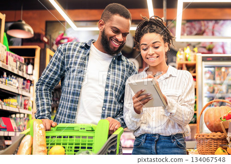 Grocery Shopping. Black Family Couple Buying Food And Fruits Taking Notes In Checklist Choosing Groceries Together In Modern Supermarket. Spouses Buy Fresh Organic Vegetables In Store Grocery Shopping. Black Family Couple Buying Food And Fruits Taking Notes In Checklist Choosing Groceries Together In Modern Supermarket. Spouses Buy Fresh Organic Vegetables In Store 134067548