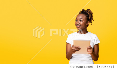 Exciting application. Interested black girl with digital tablet looking at free space over yellow background, panorama Exciting application. Interested black girl with digital tablet looking at free space over yellow background, panorama 134067741
