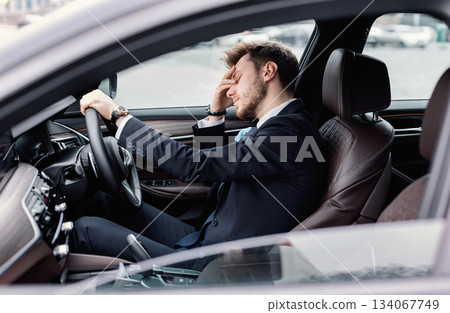 Young bearded business man sitting in car very upset and stressed after hard failure and moving in traffic jam Young bearded business man sitting in car very upset and stressed after hard failure and moving in traffic jam 134067749