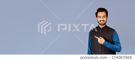 Handsome young Indian man smiling and pointing aside on lilac background Handsome young Indian man smiling and pointing aside on lilac background 134067808
