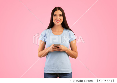 Amazing Application. Portrait of happy smiling young woman using smartphone standing isolated over yellow studio background, looking at camera, holding gadget, copy space. Lady chatting online 134067851
