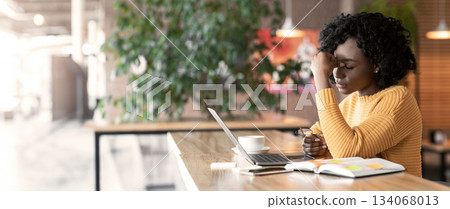Tired african american girl sitting in cafe, looking for job online, using laptop, rubbing her nose bridge, empty space Tired african american girl sitting in cafe, looking for job online, using laptop, rubbing her nose bridge, empty space 134068013