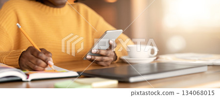 Cropped photo of black woman taking notes and using smartphone Cropped photo of black woman taking notes and using smartphone 134068015