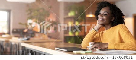 Excited afro girl drinking tea at cafe and dreaming about prosperous future, copy space 134068031