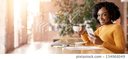 Happy black girl chatting with friends on smartphone while spending time at cafe, having cup of coffee, free space Happy black girl chatting with friends on smartphone while spending time at cafe, having cup of coffee, free space 134068049