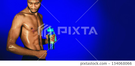 Fitness Lifestyle. African American Guy Looking At Muscles After Workout Holding Bottle Of Water Over Blue Studio Background. Free Space 134068066