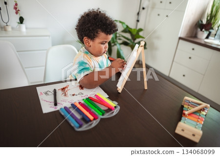 Toddler drawing on easel with colorful markers at home Toddler drawing on easel with colorful markers at home 134068099