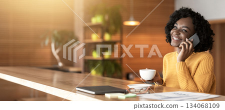 Smiling young black businesswoman drinking coffe at cafe, having conversation by phone, copy space 134068109