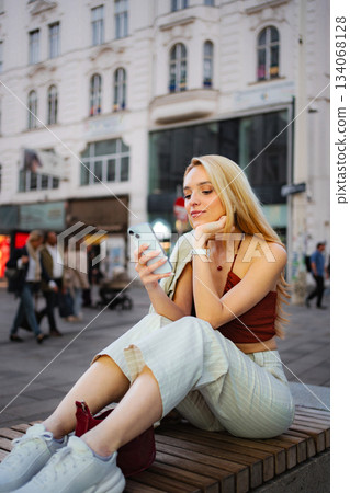 Young woman using smartphone sitting on bench in Vienna 134068128