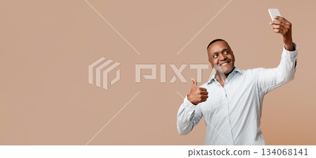 Modern african middle aged man making selfie and gesturing like, orange background, free space Modern african middle aged man making selfie and gesturing like, orange background, free space 134068141