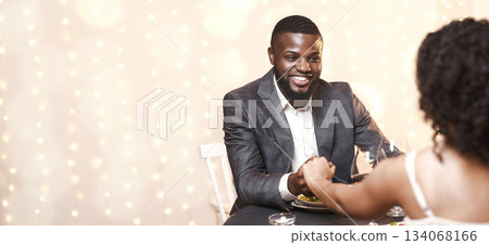 Happy black guy courting his woman, having date in fancy restaurant, man holding woman hand Happy black guy courting his woman, having date in fancy restaurant, man holding woman hand 134068166