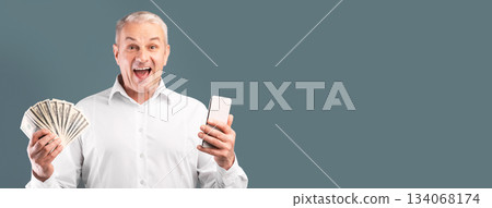 Making Money Via Internet. Excited mature man showing bunch of money, holding smartphone, free space, blue studio wall Making Money Via Internet. Excited mature man showing bunch of money, holding smartphone, free space, blue studio wall 134068174