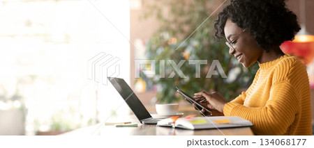 Happy afro girl freelancer using mobile phone, working with laptop in cafe, side view, copy space Happy afro girl freelancer using mobile phone, working with laptop in cafe, side view, copy space 134068177