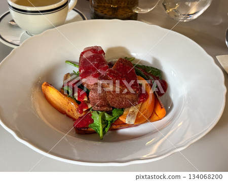 Meat with vegetables and berry sauce on a white plate. Culinary craftsmanship, contrast of colors, and fine dining mood through modern plating. Meat with vegetables and berry sauce on a white plate. Culinary craftsmanship, contrast of colors, and fine dining mood through modern plating. 134068200