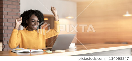 Black girl celebrating success in front of laptop at cafe, clenching fists and screaming, found good job, copy space 134068247