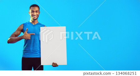 Cheerful Fitness Guy Holding Blank White Board For Text Pointing Finger At It Standing On Blue Background. Mockup, Studio Shot Cheerful Fitness Guy Holding Blank White Board For Text Pointing Finger At It Standing On Blue Background. Mockup, Studio Shot 134068251
