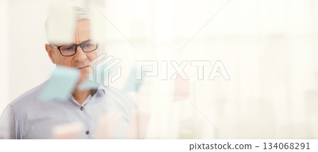 Business Strategy. Pensive Senior Manager In Specs Looking At Sticky Notes On Window At Office, Copyspace 134068291