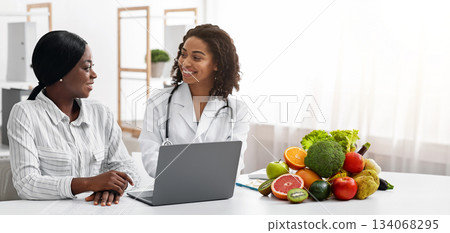 Smiling black lady doctor chatting with female patient at clinic, dietology and nutririon concept Smiling black lady doctor chatting with female patient at clinic, dietology and nutririon concept 134068295