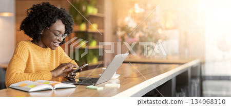 Happy black girl using mobile phone, working with laptop in cafe, side view, copy space Happy black girl using mobile phone, working with laptop in cafe, side view, copy space 134068310