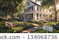 A white two-story house with black shutters sits on a grassy lot. The house has a large front porch with a swing. Lush green landscaping surrounds the house, with flowers blooming in the front yard. A white two-story house with black shutters sits on a grassy lot. The house has a large front porch with a swing. Lush green landscaping surrounds the house, with flowers blooming in the front yard. 134068736
