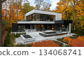 A striking modern house features large windows that reflect the colorful autumn foliage. The surrounding trees display vivid reds and yellows, creating a tranquil atmosphere perfect for relaxation. A striking modern house features large windows that reflect the colorful autumn foliage. The surrounding trees display vivid reds and yellows, creating a tranquil atmosphere perfect for relaxation. 134068741