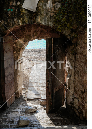 Close-up photo of a doorway opening to reveal a view of the sea. The image emphasizes architectural details of the door and the surrounding wall while showcasing the coastal scenery. Suitable for Close-up photo of a doorway opening to reveal a view of the sea. The image emphasizes architectural details of the door and the surrounding wall while showcasing the coastal scenery. Suitable for 134069063