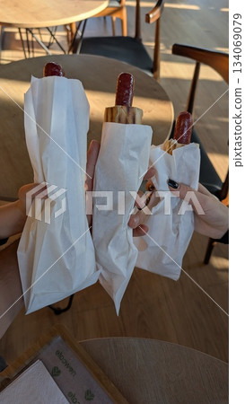 sharing quick snacks at sunny cafe, people savoring warm hotdogs amid cheerful outdoor atmosphere 134069079
