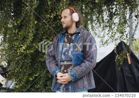 Person with headphones relaxing outdoors in layered clothing scene Person with headphones relaxing outdoors in layered clothing scene 134070210