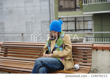 young woman with blue beanie listening to music on bench young woman with blue beanie listening to music on bench 134070213