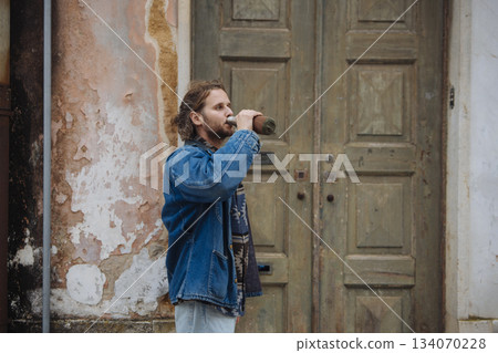 Man relaxes with beverage beside aged doorway during urban stroll Man relaxes with beverage beside aged doorway during urban stroll 134070228